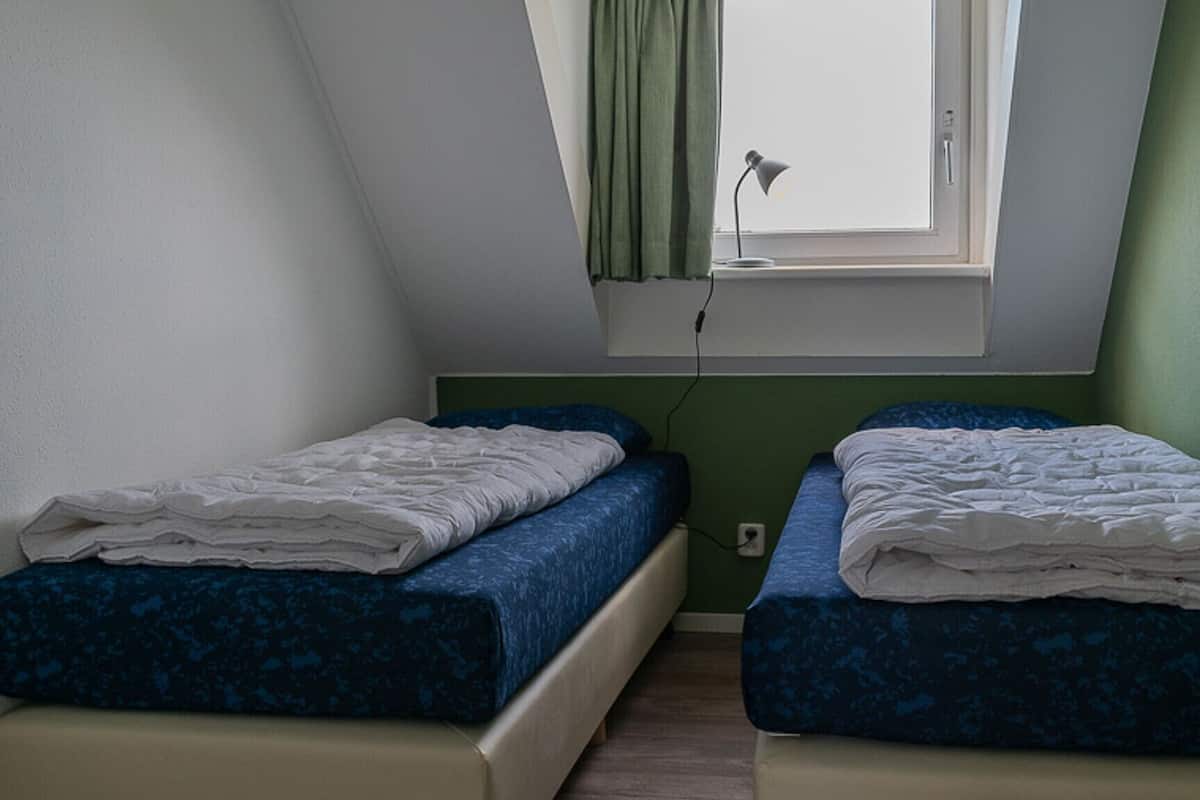 A small, single-room with two beds, a window with a lamp, and a green wall.