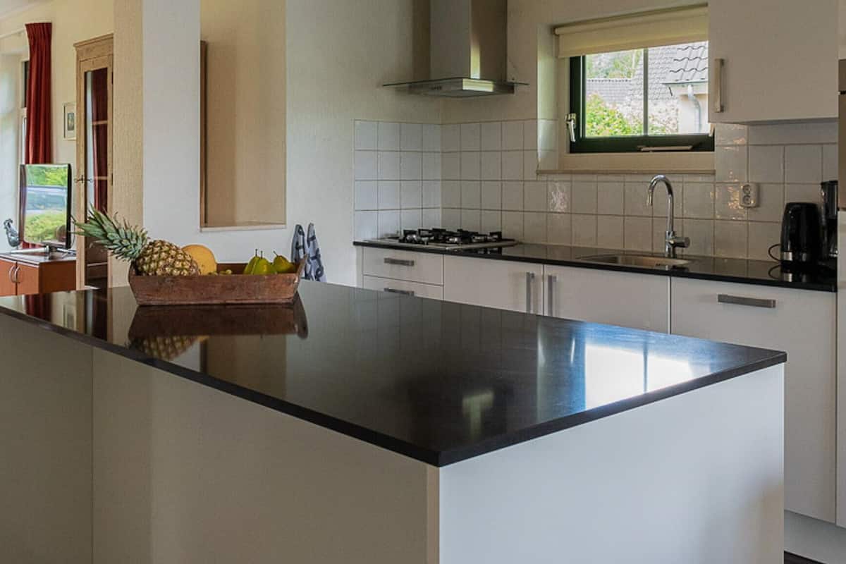 A modern kitchen with a large island, white cabinetry, a stainless steel sink, and a built-in oven.