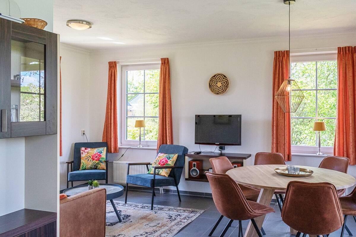 A modern living room with a dining area, large windows with curtains, a flat-screen TV, and a fireplace.