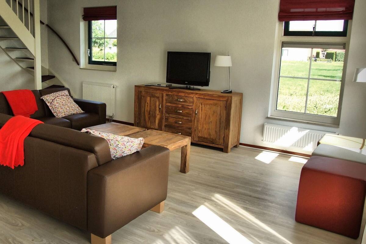A living room with a sofa, a wooden cabinet, a TV, and a window with a view of greenery.