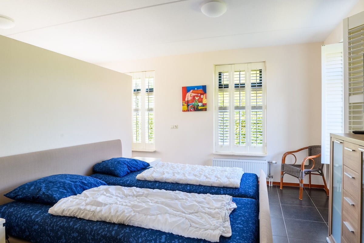 A bedroom with two beds, a TV, a chair, and a radiator.