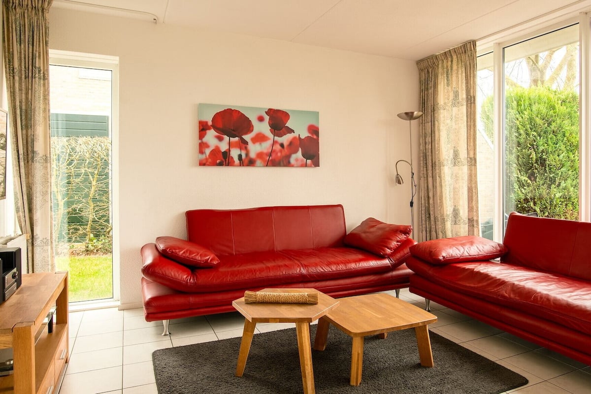 A living room with a red leather sofa, a wooden coffee table, and a painting of red flowers on the wall.