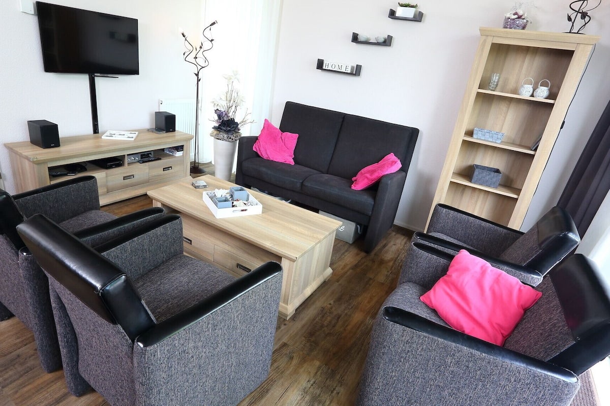 A modern living room with a black sofa, grey armchairs, a wooden coffee table, and a TV mounted on the wall.