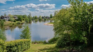 Una vista tranquila de un lago, con una casa a la izquierda y abundante vegetación a la derecha.
