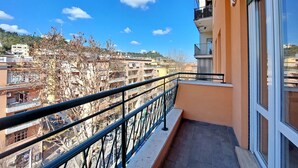 Un balcon doté d’une rambarde en métal, donnant sur un quartier résidentiel composé de plusieurs immeubles, avec une colline en arrière-plan.