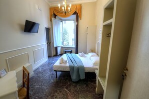 A hotel room with a bed, a television mounted on the wall, a window with curtains, and a chandelier. - Palazzo Alibrandi (Civitavecchia)