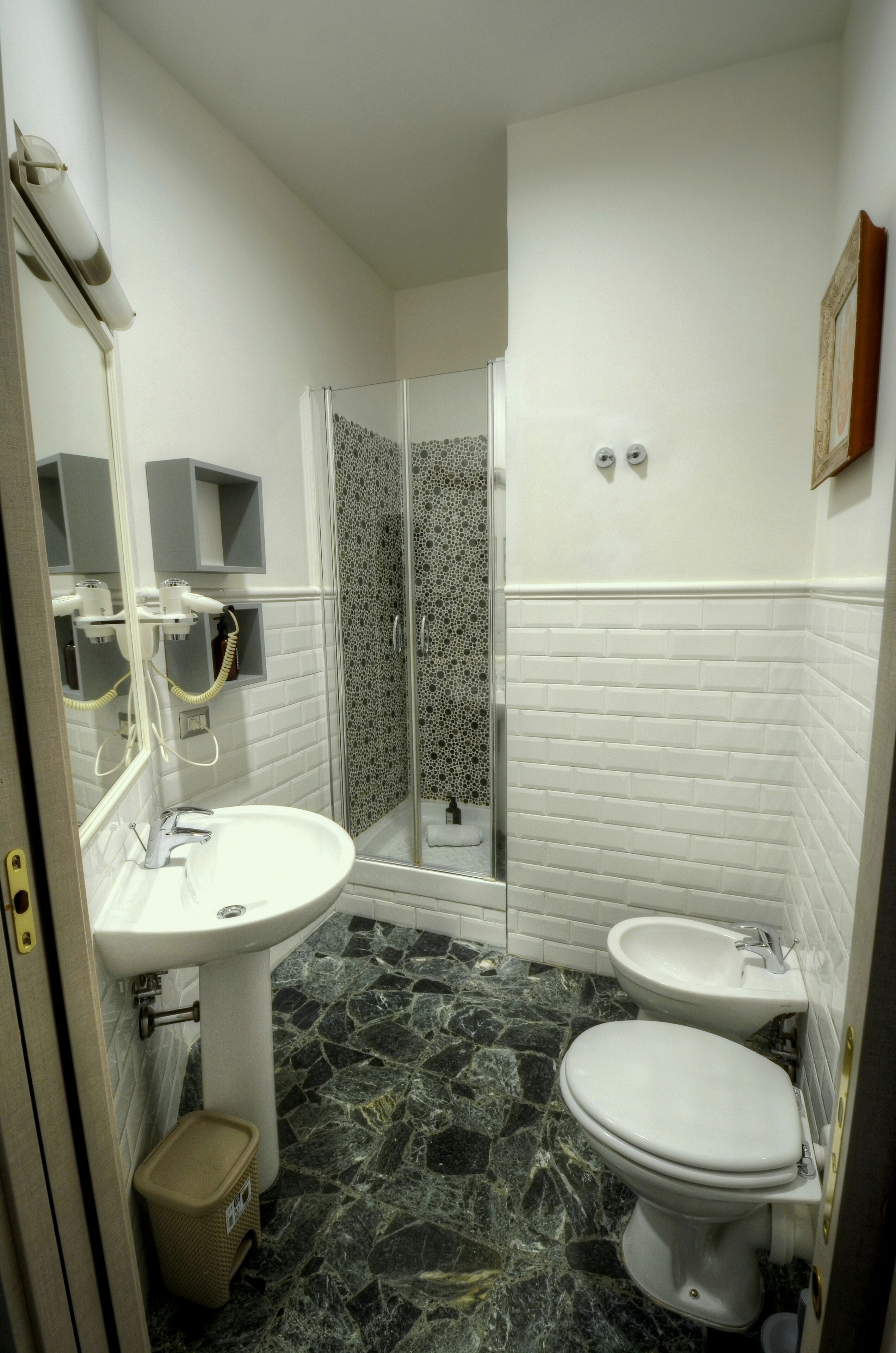 Un baño con lavamanos pedestal, inodoro y ducha con mampara de vidrio.