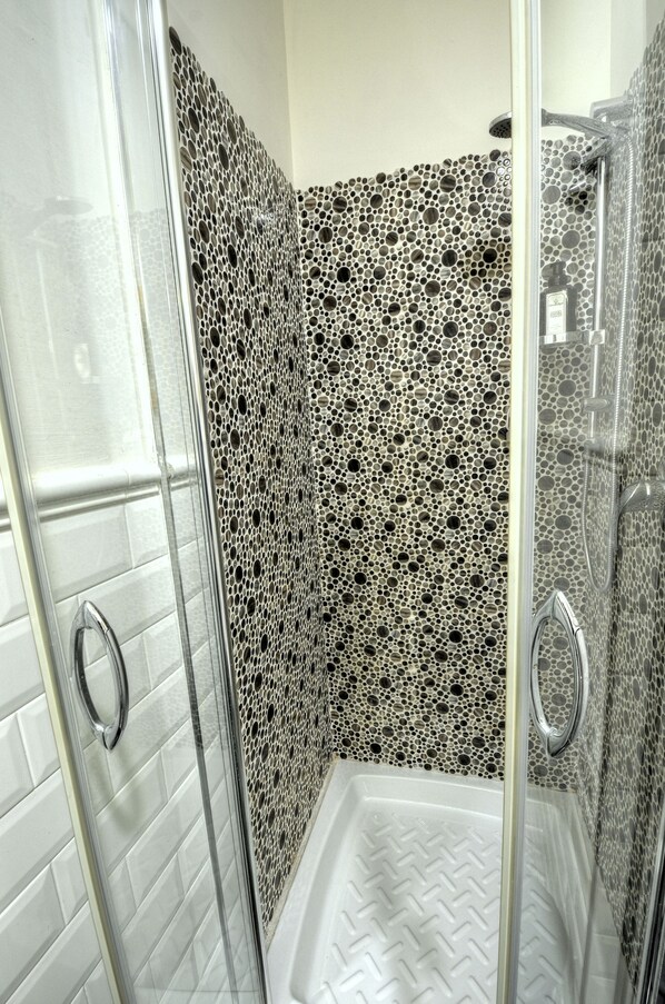 A shower with a patterned wall and a clear glass door.