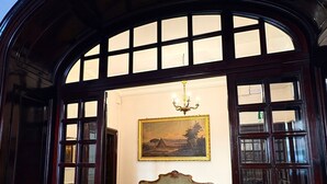 An interior with a large arched doorway, a green sofa, a chandelier, and a painting on the wall. - Palazzo Alibrandi (Civitavecchia)