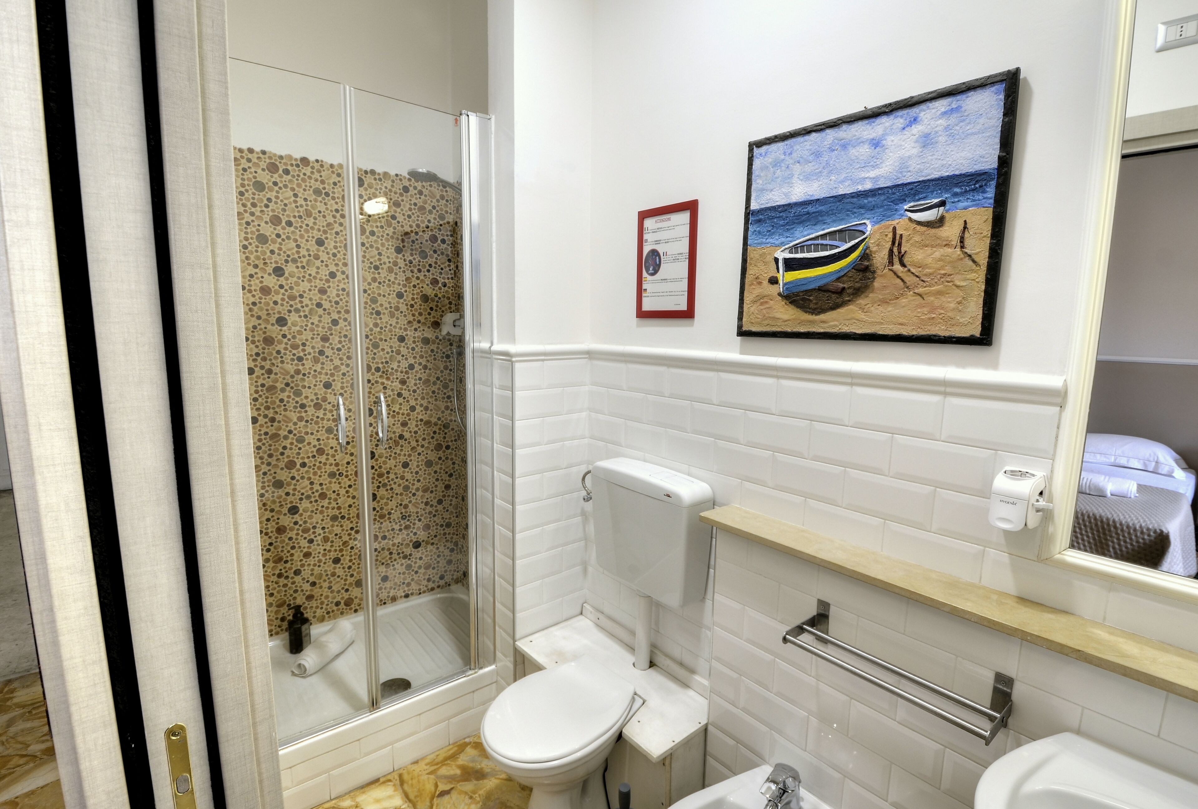 Un baño con ducha de vidrio, inodoro, lavamanos y un cuadro con una playa.