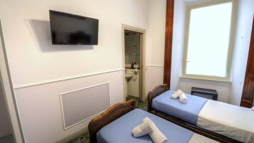 Une chambre d’hôtel avec deux lits, un téléviseur fixé au mur et une fenêtre laissant entrer la lumière naturelle.