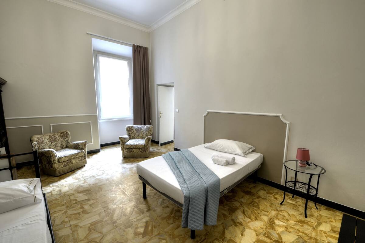A hotel room with a bed, two armchairs, a small table, and a window with curtains.