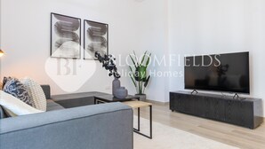 Een moderne woonkamer met een grijze bank, een zwart tv-meubel en twee abstracte schilderijen aan de muur.