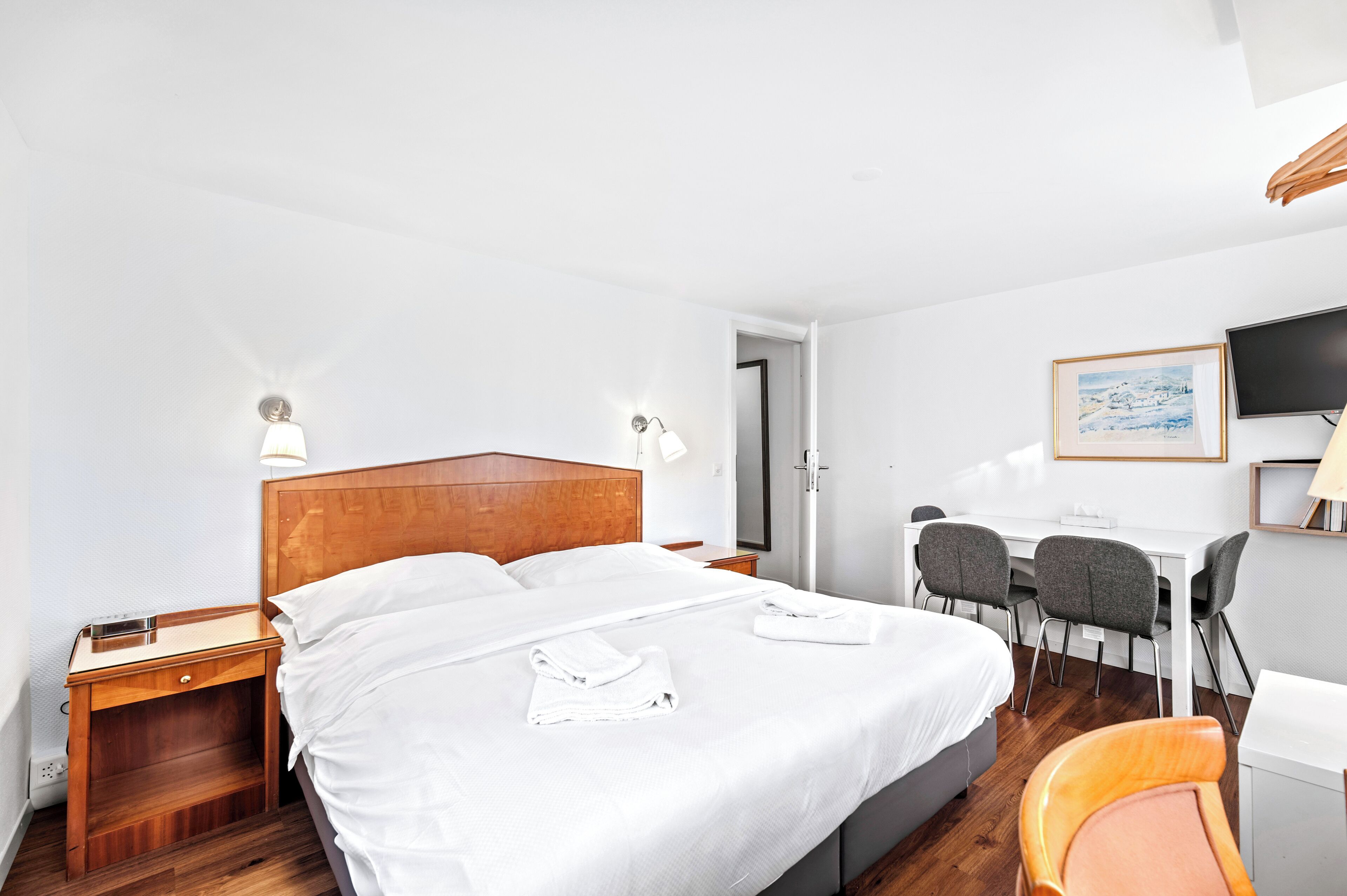 Habitación de hotel con cama, mesita de noche, lámpara, escritorio, sillas y televisor.