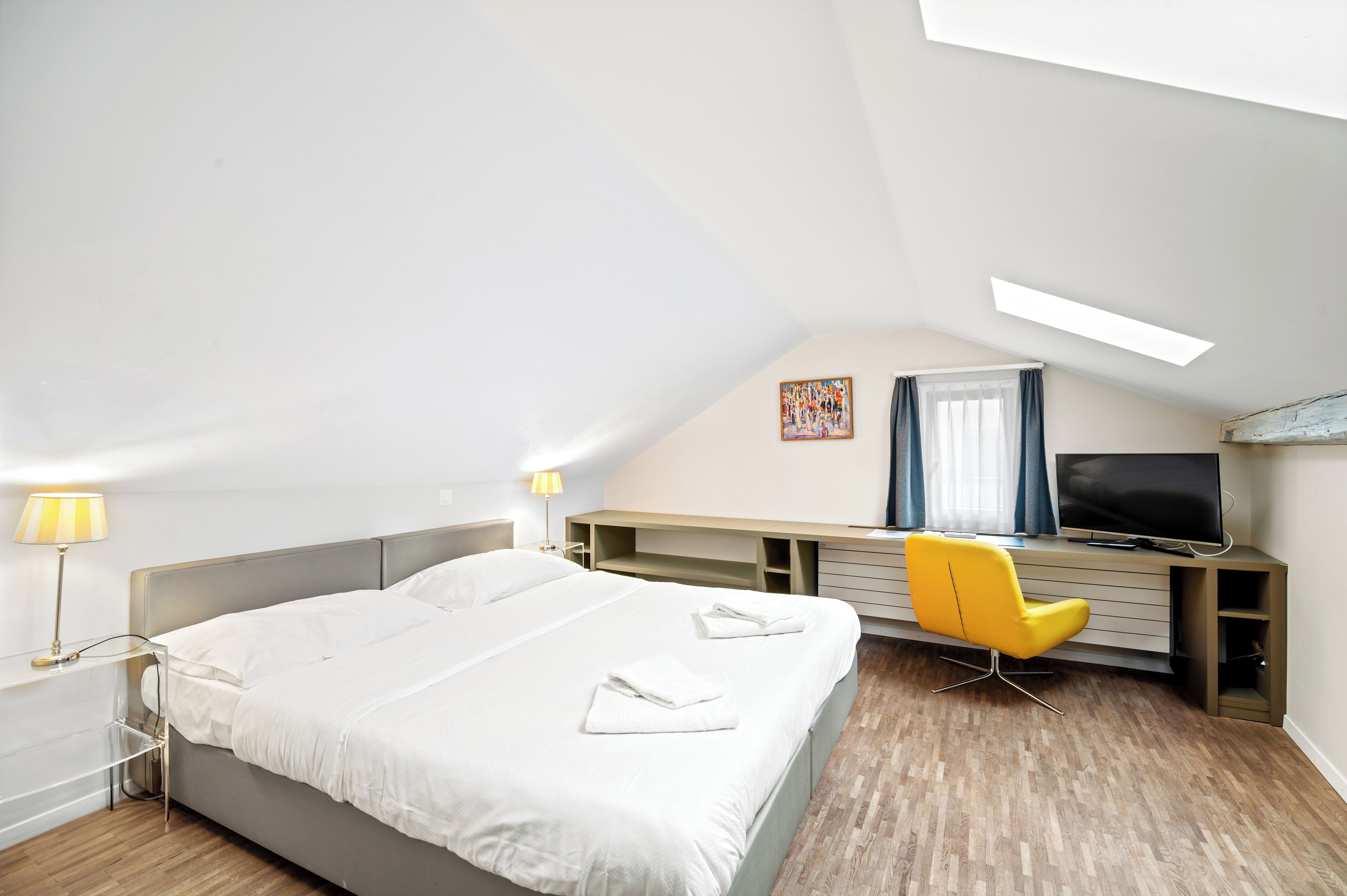 Une chambre d’hôtel moderne dotée d’un grand lit, d’un bureau avec un ordinateur, d’une télévision et d’une grande fenêtre laissant entrer beaucoup de lumière.