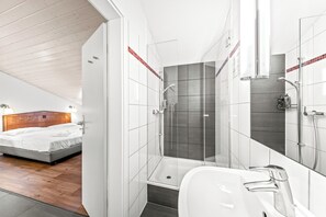 A modern bedroom with a wooden headboard bed and a separate shower area with a glass enclosure and a large mirror. -  Hine Adon Fribourg City Aparthotel Self checkin (Fribourg)