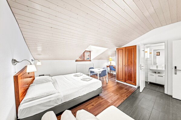 A modern hotel room with a wooden ceiling, a large bed, a desk, and a bathroom. -  Hine Adon Fribourg City Aparthotel Self checkin (Fribourg)