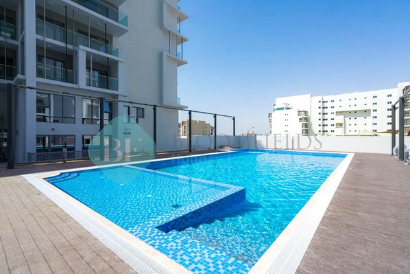 A rectangular swimming pool with a tiled edge, surrounded by a wooden deck. - Bloomfields City STU In Oasis (Abu Dabi)