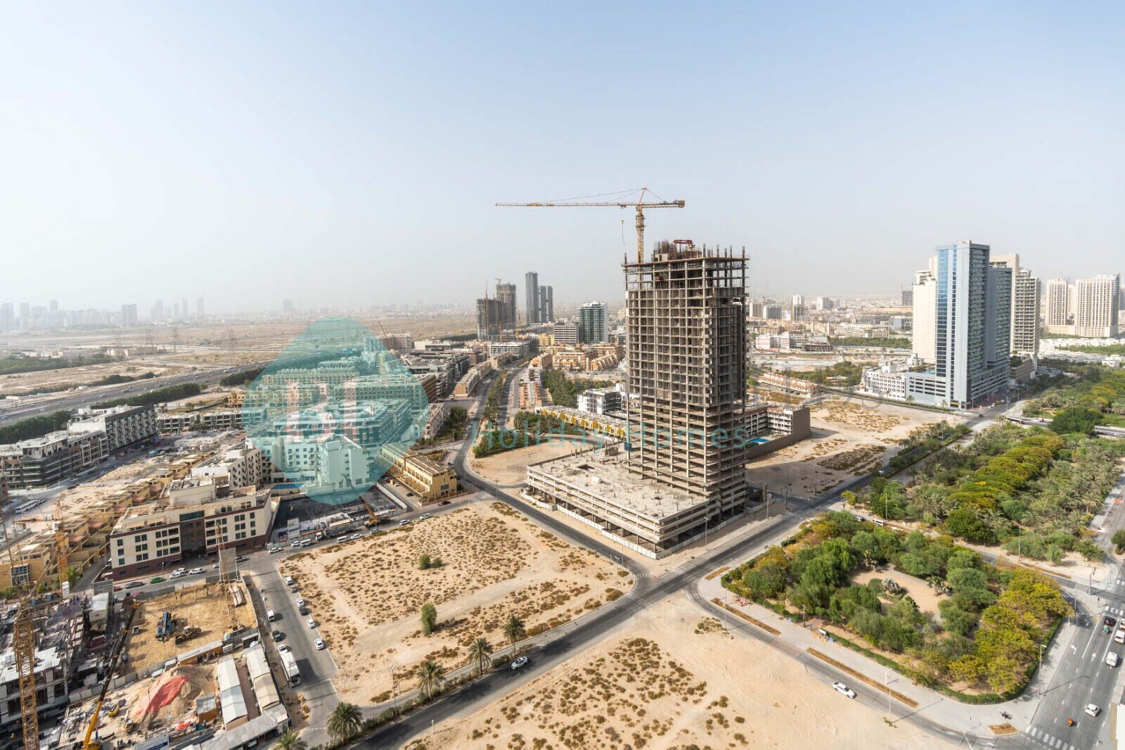 A high-rise building under construction with a crane, surrounded by other buildings and roads.