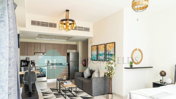 A modern living room with a sofa, coffee table, and a TV. There is a kitchen in the background with a fridge and a microwave.