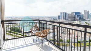 A balcony with wicker chairs and a glass table overlooking a cityscape with modern buildings and a road.