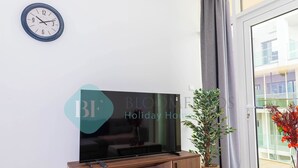Moderni olohuone, jossa on litteänäyttöinen televisio puisen TV-tason päällä, seinäkello ja ikkunan vieressä oleva ruukkukasvi.