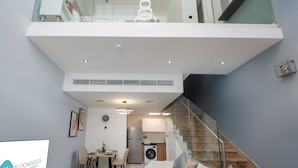 A modern apartment with a dining area, kitchen, and a glass staircase. - Bloomfields Premium 1BR Duplex in Rukan (Dubai)