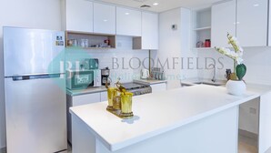 A modern kitchen with white cabinetry, a central island, and stainless steel appliances. - Bloomfields Metropolitan 3BR In Bridges (Abu Dabi)