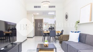 A modern living room with a sofa, a dining table, and a kitchen in the background. - Bloomfields Stylish 2Br in Rukan (Dubai)