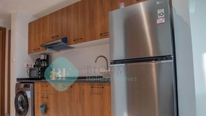 Een moderne keuken met houten kastjes, een roestvrijstalen koelkast, een wasmachine en een koffiezetapparaat.