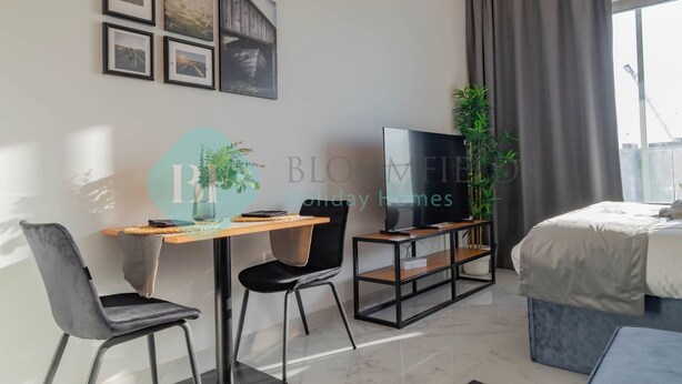 Een moderne hotelkamer met een bed, een televisie, een bureau met stoel en een groot raam met gordijnen.