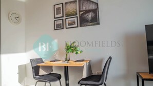 Een eethoek met een houten tafel, twee zwarte stoelen en een klok aan de muur.