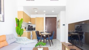 A modern living room with a sofa, a coffee table with a bonsai tree, and a dining area with a table and chairs. - Bloomfields Iconic 1BR in Oasis Masdar (Abu Dabi)