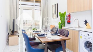 A modern kitchen with a washing machine, dining table with chairs, and a view of the city.