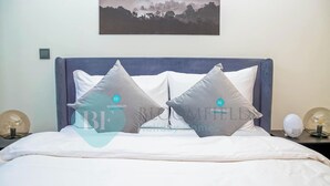A neatly made bed with two pillows, a blue headboard, and two bedside lamps. - Bloomfields Cozy STU Azizi Riviera Meydan (Dubai)