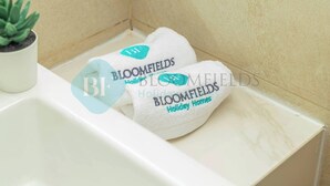 A bathroom with a white sink, a small potted plant, and two towels with 'Bloomfields Holiday Homes' branding. - Bloomfields Cozy STU Azizi Riviera Meydan (Dubai)