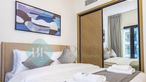 Una habitación de hotel con cama, almohadas, una toalla doblada, un cuadro y una puerta corredera.