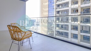 Un balcón con barandilla de vidrio, una silla de mimbre y vistas a un edificio de gran altura.