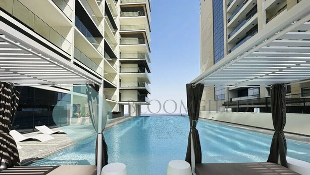 Un área de piscina interior moderna con paredes de vidrio transparente, sillas de descanso y vistas al cielo.