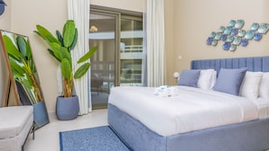Ein modernes Schlafzimmer mit einem großen Bett, einer Zimmerpflanze, einem Spiegel und Blick auf den Balkon.