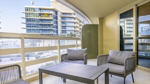 Ein Balkon mit Tisch und zwei Stühlen, Blick auf ein modernes Gebäude und eine Glastür.