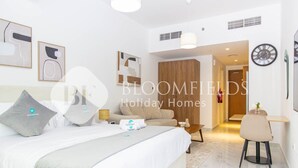 A modern hotel room with a large bed, a sofa, a dining area, and a hallway leading to another room. - Bloomfields Pretty STU in Oasis (Abu Dabi)