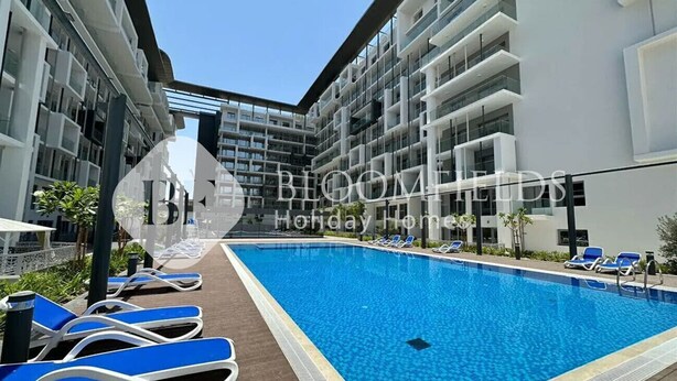 A modern hotel with a central swimming pool, multiple balconies, and sun loungers. - Bloomfields Pretty STU in Oasis (Abu Dabi)