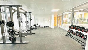 A gym with weightlifting equipment, large windows, and a view of the outside. - Bloomfields Pretty STU in Oasis (Abu Dabi)