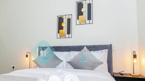 Un lit bien fait, avec des serviettes pliées, une lampe de chevet et deux œuvres d’art accrochées au mur au-dessus.