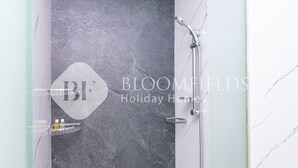 Un baño con pared de mármol gris, ducha con cabezal de ducha manual y un pequeño estante con artículos de aseo.