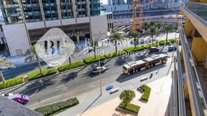 Un edificio moderno con fachada de vidrio, una carretera bien mantenida con palmeras y una grúa de construcción al fondo.