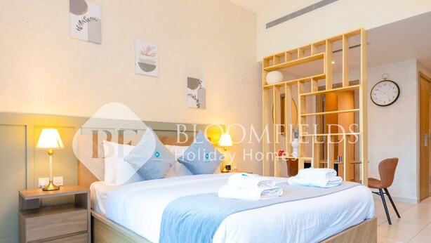 Una habitación de hotel moderna con una cama grande, mesitas de noche con lámparas, cabecero de madera y una estantería empotrada.
