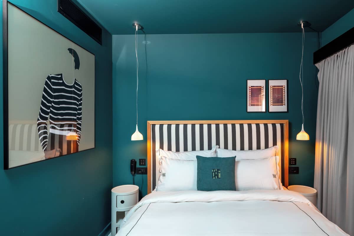 Quarto moderno com cabeceira listrada, uma cama grande, mesas de cabeceira e uma luminária fixada na parede.