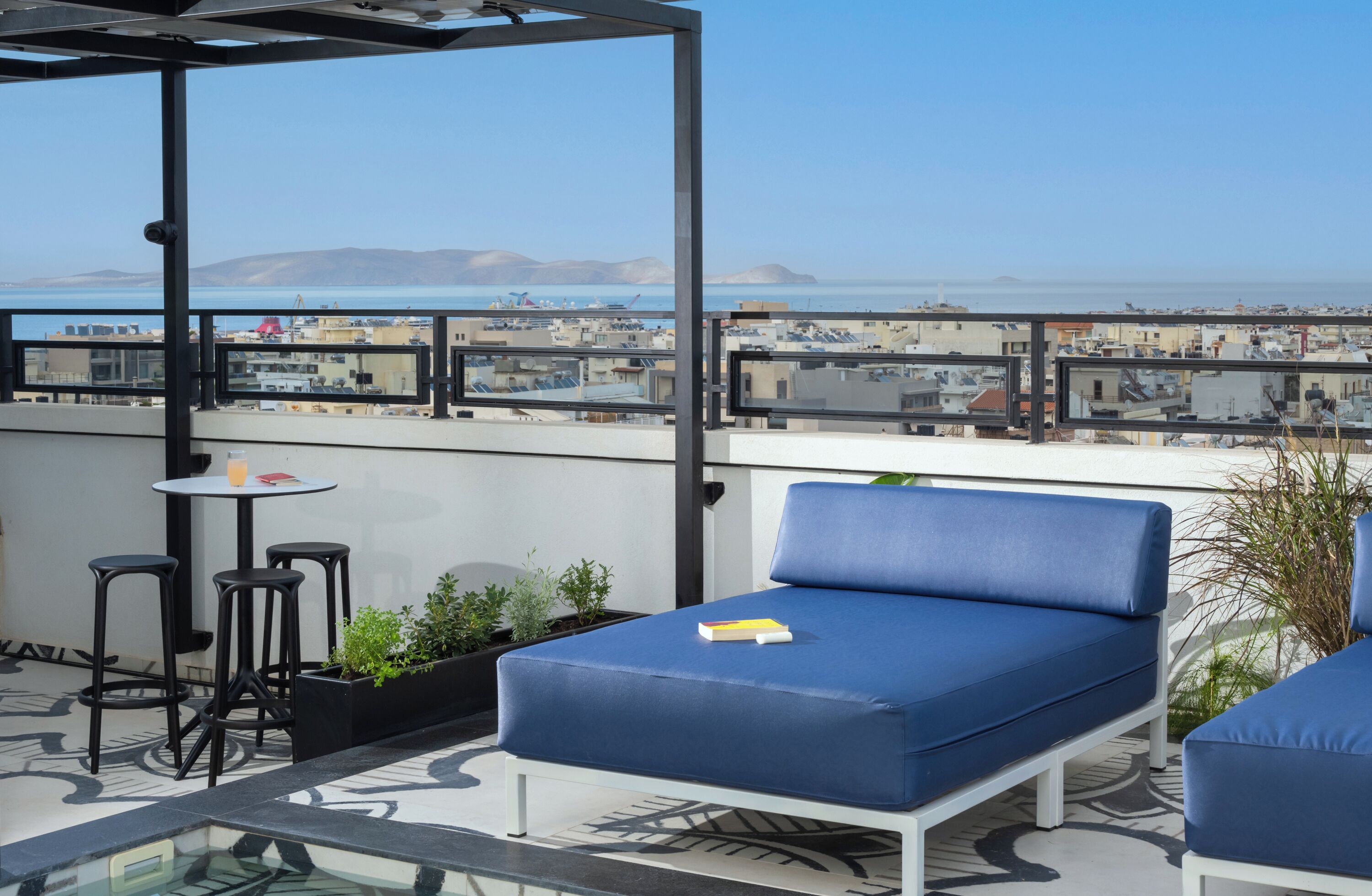 Une terrasse sur le toit avec un canapé bleu, deux tabourets de bar, une petite table et des plantes en pot.